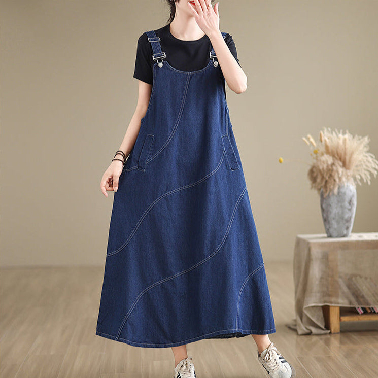 Person wearing a blue denim dress over a black shirt in a room with a table and vase.
